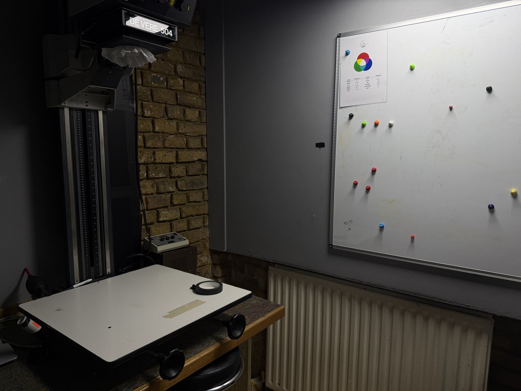 A darkroom at Chan Photo Lab with a De Vere 504 enlarger and colour correction chart